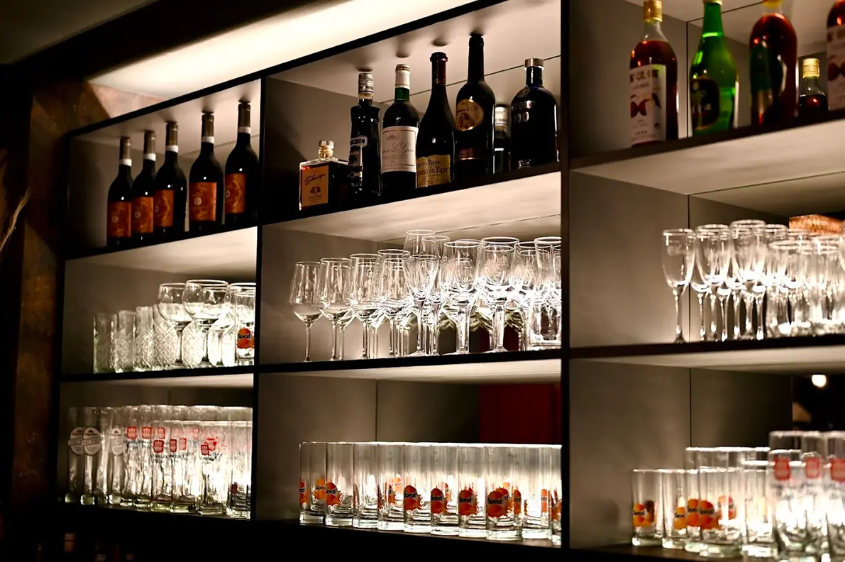 Blick zur Theke des Restaurants. Beleuchtete Wandregale mit verschiedenen Gläsern und Flaschen mit alkoholischen Getränken.