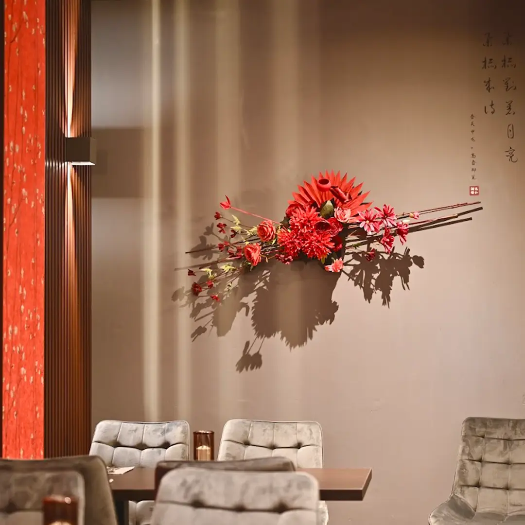 Blumengesteck bestehend aus verschiedenen roten Blumen an einer Wand im Restaurant.